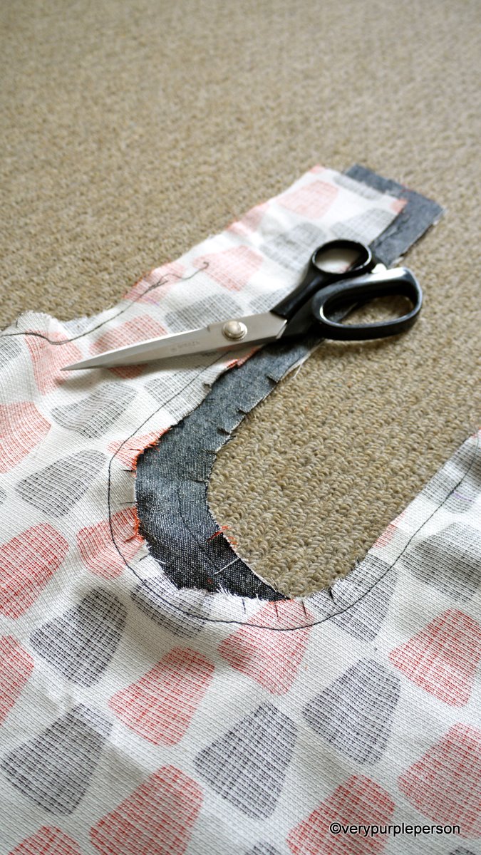 Real photograph of clipped inward-curving allowances, nearby stitching and scissors. The photographer’s copyright credit remains at the bottom. Visible operation only, not bag engineering dimensions or a safe cut-depth specification.
