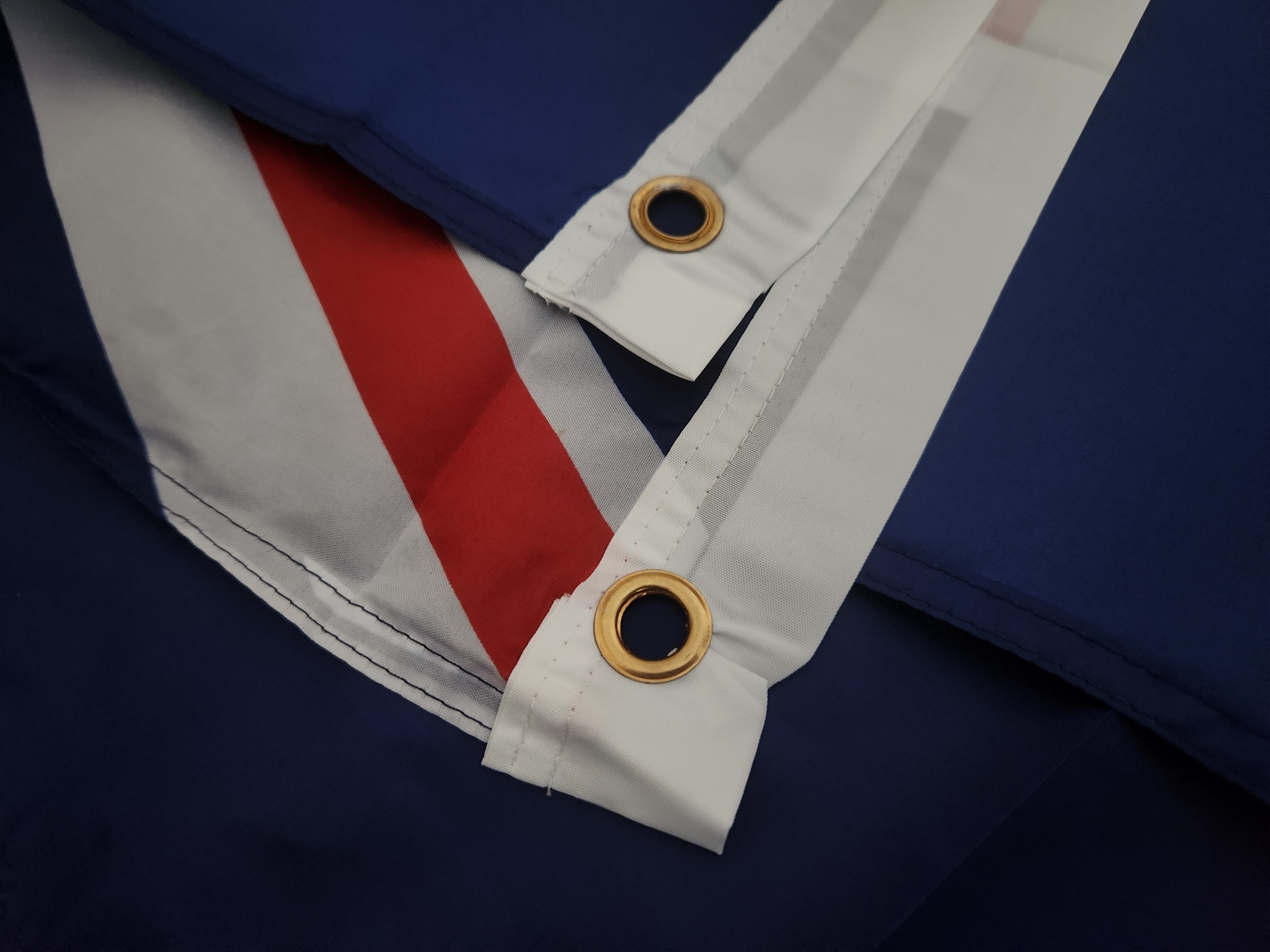 Real photograph of two installed eyelets and adjacent stitching on a folded New Zealand flag. An installation-interface example, not a bag case or evidence of metal composition, setting parameters or strength.