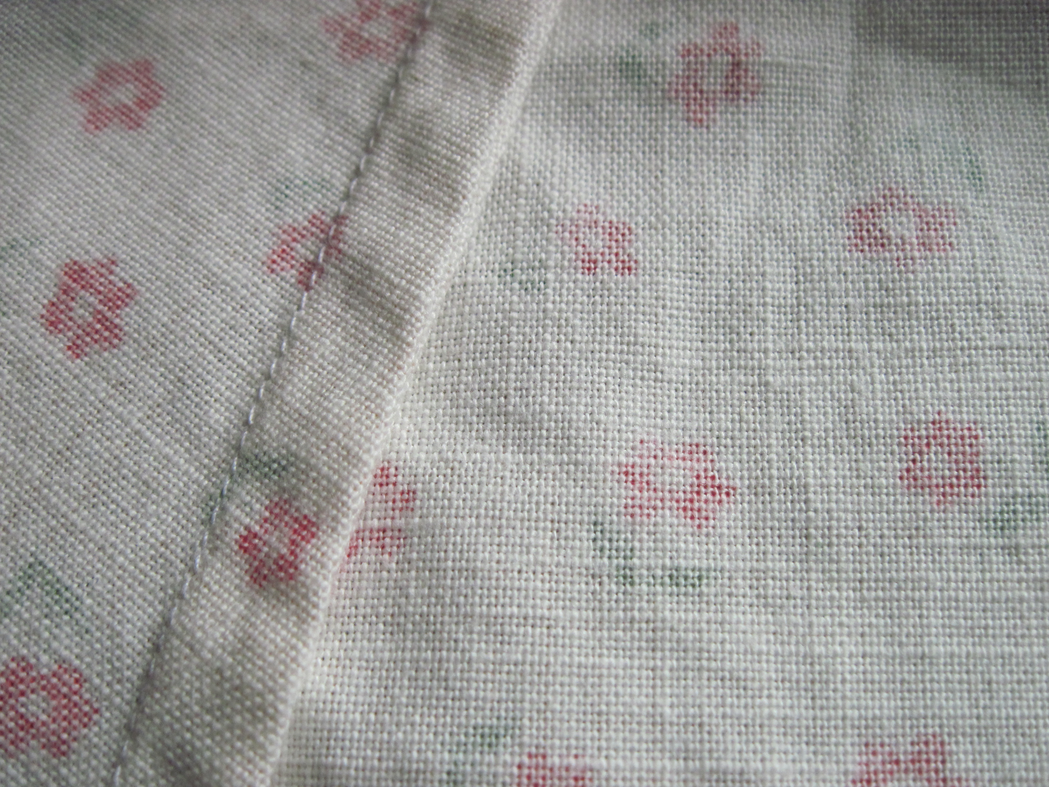 Real photograph of a folded seam and stitches on pale printed fabric, identified by its source as a French seam. Shows appearance, not every enclosed layer, fibre content, dimensions or performance.