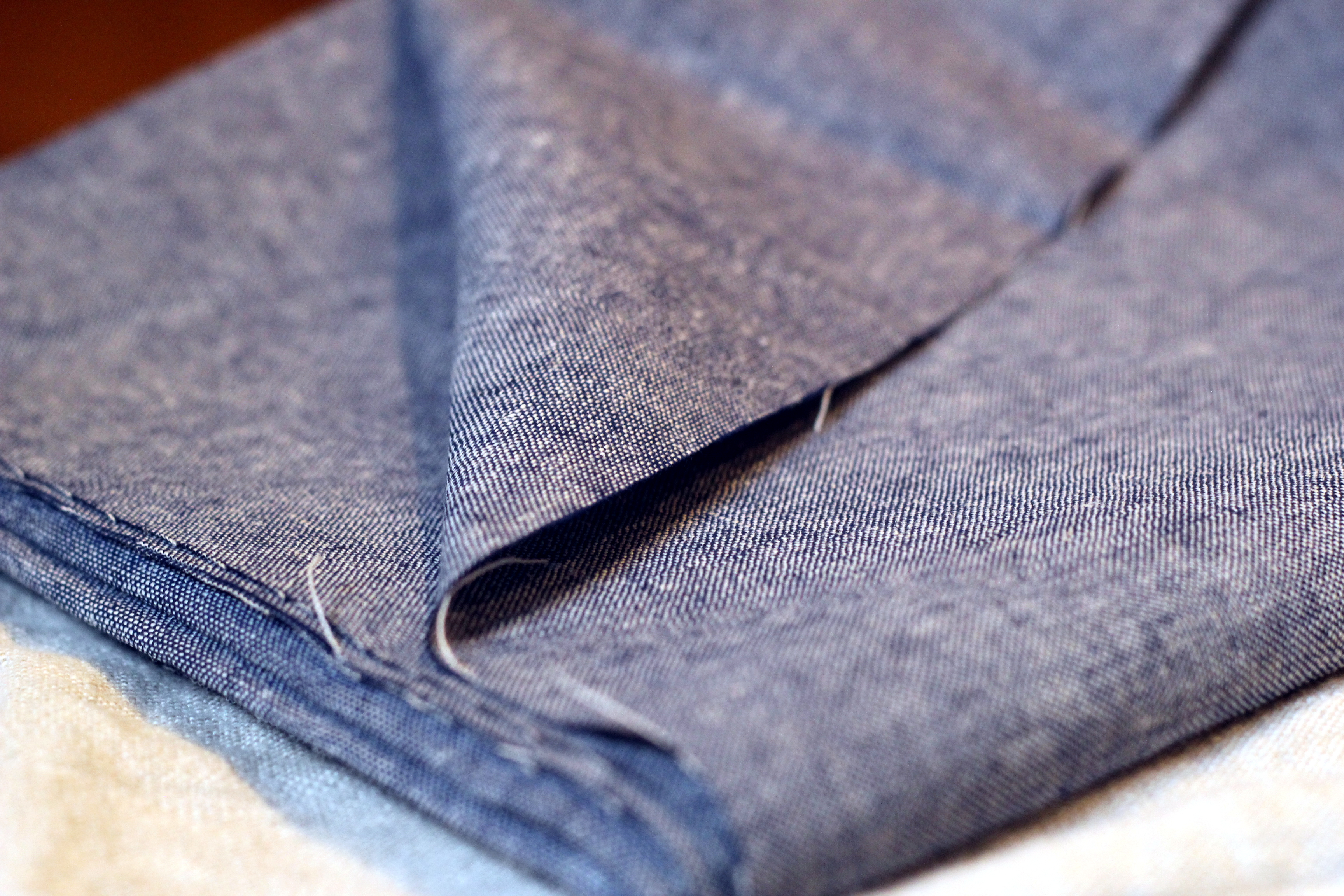 Real photograph of blue and pale yarns and folded cloth, described by its author as a cotton-linen chambray. Visible appearance only; percentages, spinning route, mass and bag suitability are unverified. Not evidence of pure linen or JKPD use. Unmodified.