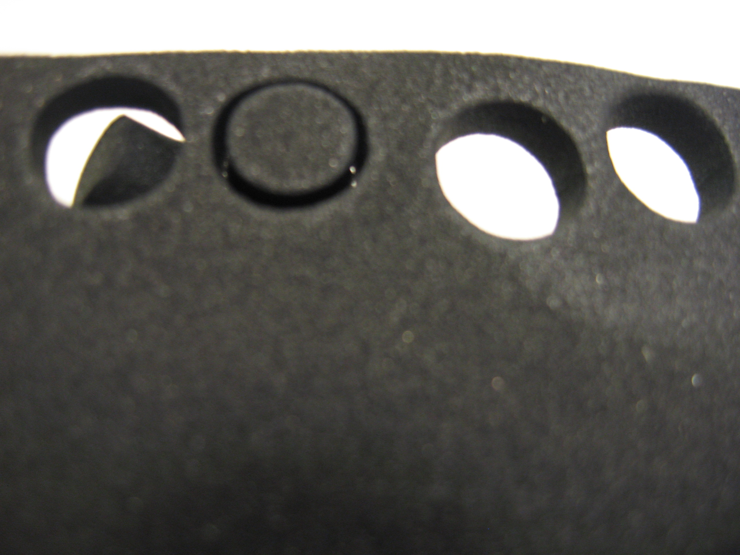 Real photograph of a dark sheet with circular punched openings and cut pieces, identified by its source as a neoprene sample. Visible geometry only; CR/SBR ratio, density, hole diameter and closed-cell content are unverified. Not JKPD or the cited suppliers’ article; unmodified.