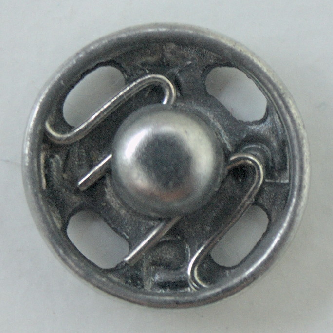 Real close-up of the fabric-facing side of a receiving snap half, with spring and peripheral openings. Does not show a paired assembly or sewn installation, or establish composition, brand or operating performance.