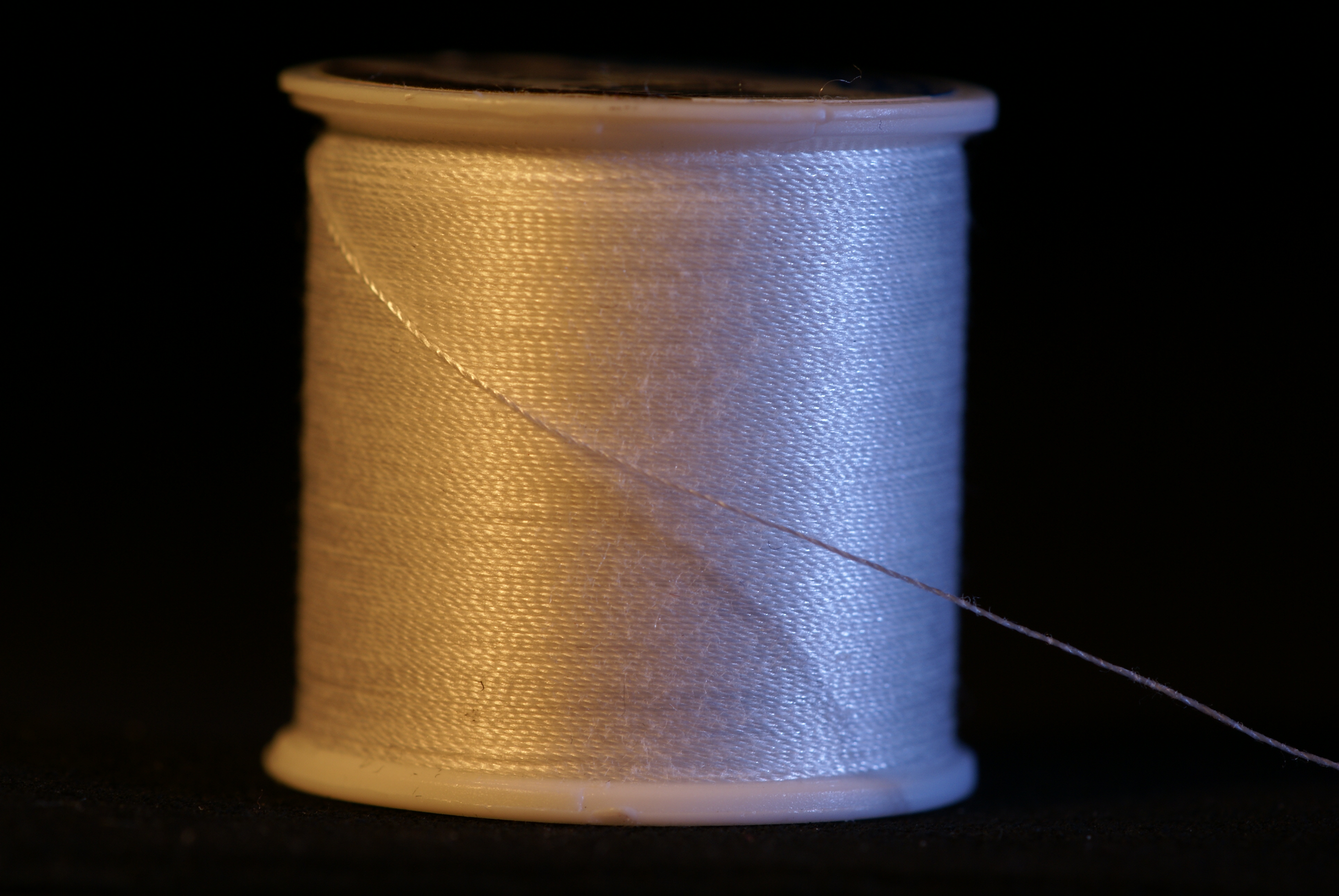 Real macro photograph of white thread and its free length, showing twist and fine surface fibres. Source describes cotton-wrapped polyester-core two-ply thread; not composition testing or evidence of Tex, strength or industrial grade. Not JKPD or the video product; unmodified.