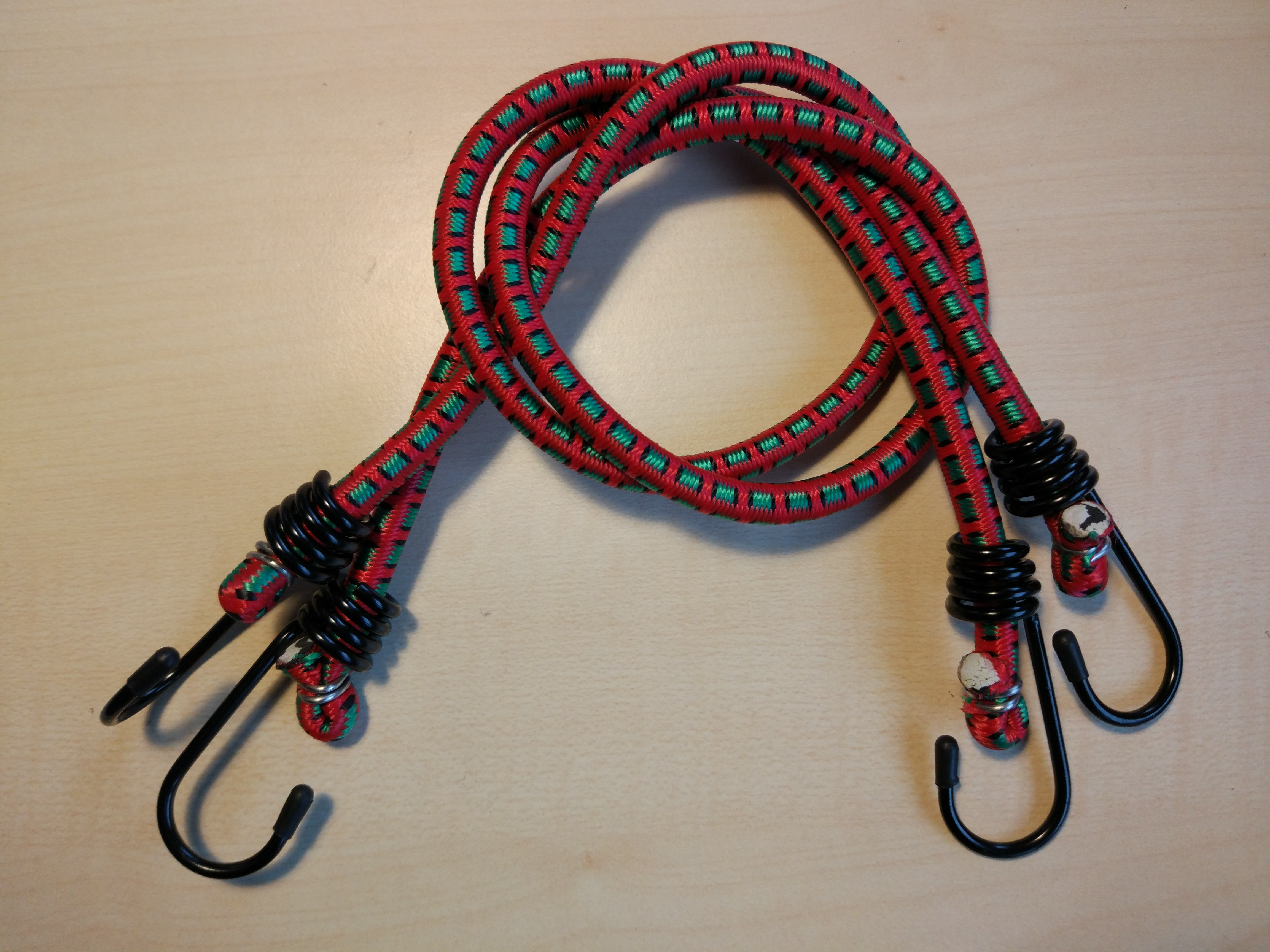 Real photograph of two covered elastic cords with hooks and visible internal bundles at the ends. Shows covering and ends only; core type, cover polymer, elongation and load capacity are unverified. Not JKPD, Marlow or the video product; unmodified.