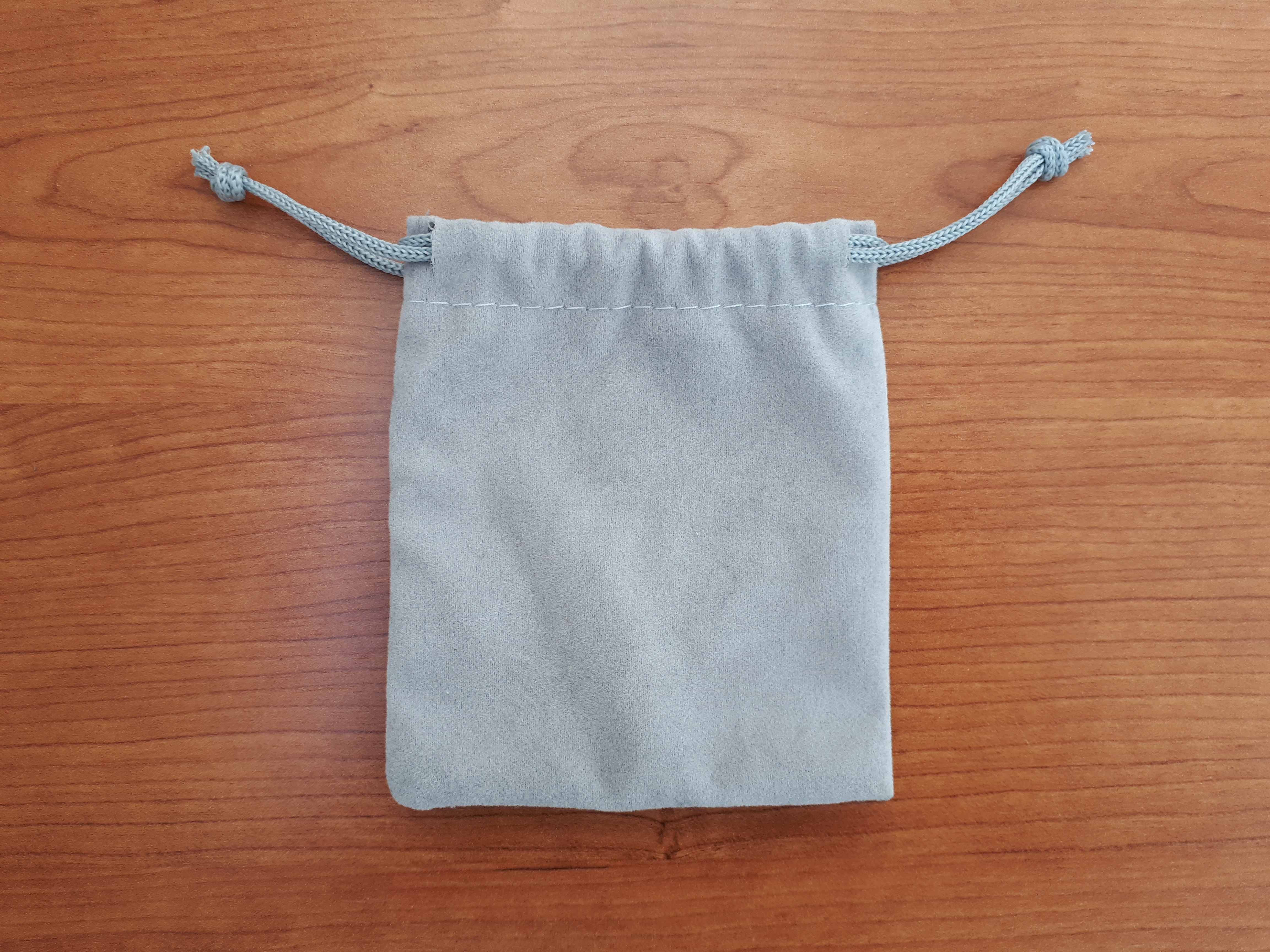 Real photograph of a grey drawstring bag mouth, horizontal stitching, side cords and knots. Locates the visible casing without establishing fibre content, usable clearance or internal layers.